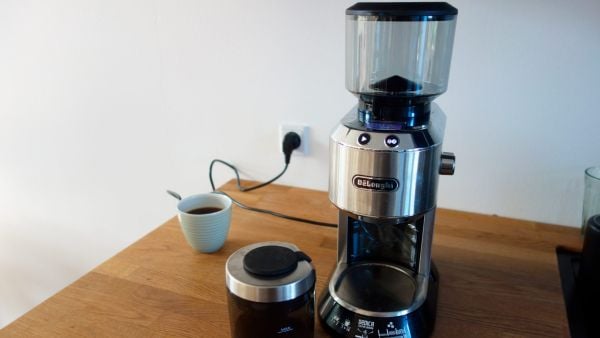 Delonghi KG521coffee grinder on kitchen table with a cup of coffee